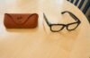 Ray-Ban Meta smart glasses Gen 2 with black frames placed on a wooden table next to a brown Ray-Ban case