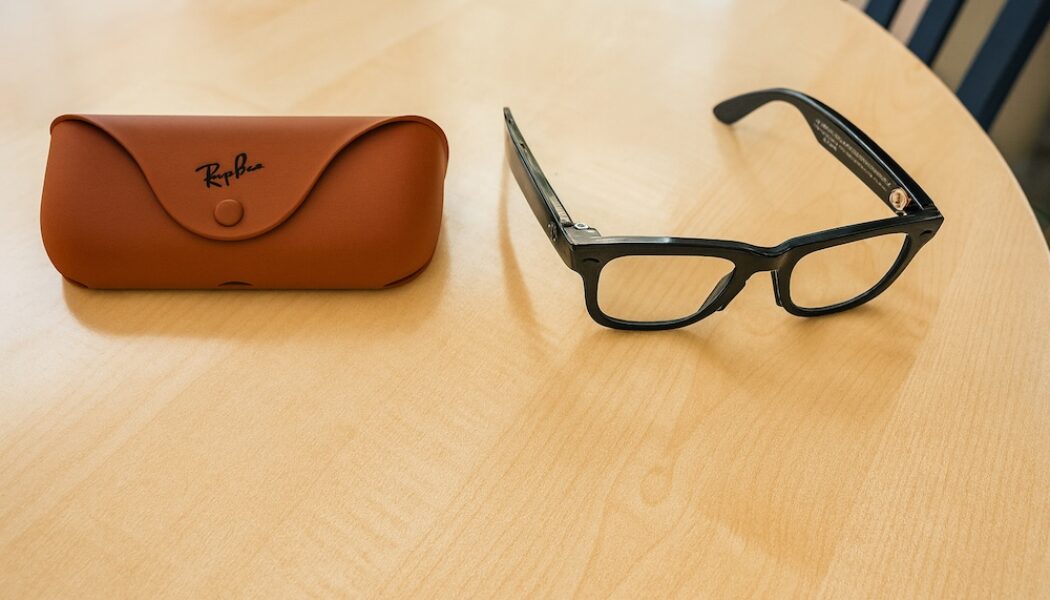 Ray-Ban Meta smart glasses Gen 2 with black frames placed on a wooden table next to a brown Ray-Ban case