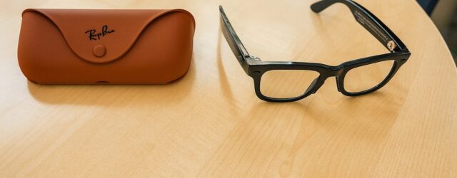Ray-Ban Meta smart glasses Gen 2 with black frames placed on a wooden table next to a brown Ray-Ban case