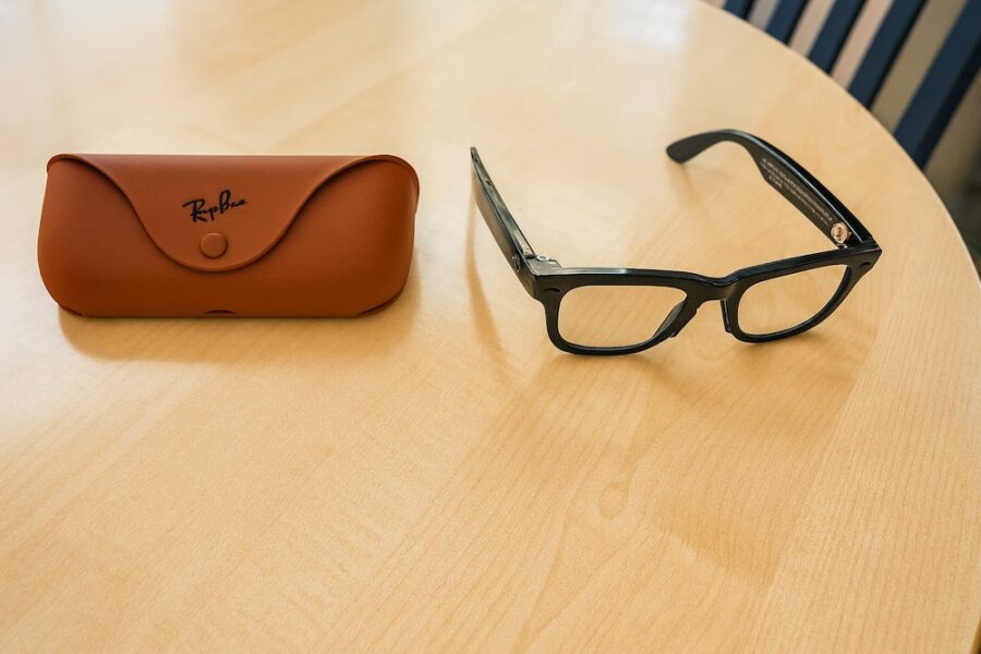 Ray-Ban Meta smart glasses Gen 2 with black frames placed on a wooden table next to a brown Ray-Ban case