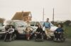 1990s family photo of Colin Hughes with siblings Ian and Lyn; three wheelchair-accessible Motability Chrysler Voyager vehicles behind them.