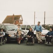 1990s family photo of Colin Hughes with siblings Ian and Lyn; three wheelchair-accessible Motability Chrysler Voyager vehicles behind them.