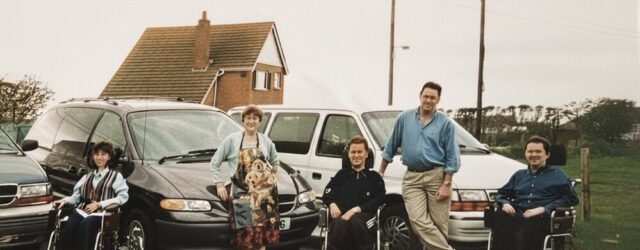 1990s family photo of Colin Hughes with siblings Ian and Lyn; three wheelchair-accessible Motability Chrysler Voyager vehicles behind them.