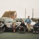 1990s family photo of Colin Hughes with siblings Ian and Lyn; three wheelchair-accessible Motability Chrysler Voyager vehicles behind them.