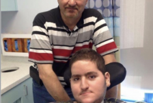 Wael Tarabishi, a disabled man using a wheelchair and breathing tube, sits in a hospital room with his father and full-time carer, Maher Tarabishi, standing behind him.