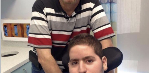 Wael Tarabishi, a disabled man using a wheelchair and breathing tube, sits in a hospital room with his father and full-time carer, Maher Tarabishi, standing behind him.