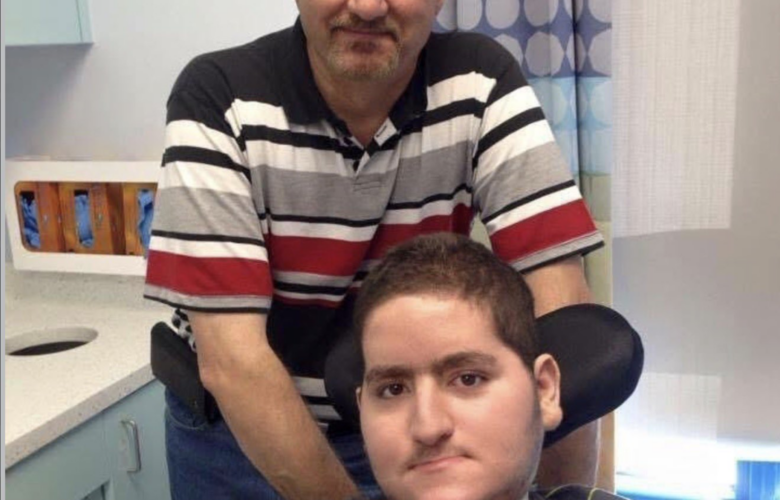 Wael Tarabishi, a disabled man using a wheelchair and breathing tube, sits in a hospital room with his father and full-time carer, Maher Tarabishi, standing behind him.