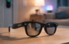 Ray-Ban Meta smart glasses on a wooden table in a modern living room with smart lighting and a smart lock in the background, illustrating smart home control potential.