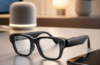 Alt text with focus keyword: Apple smart glasses beside a smartphone on a desk, with a softly lit smart speaker and lamp in the background, suggesting wearable AI and hands-free control.