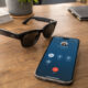 Smart glasses beside a smartphone showing an active call screen with a red end-call button, representing hands-free call controls and accessibility.